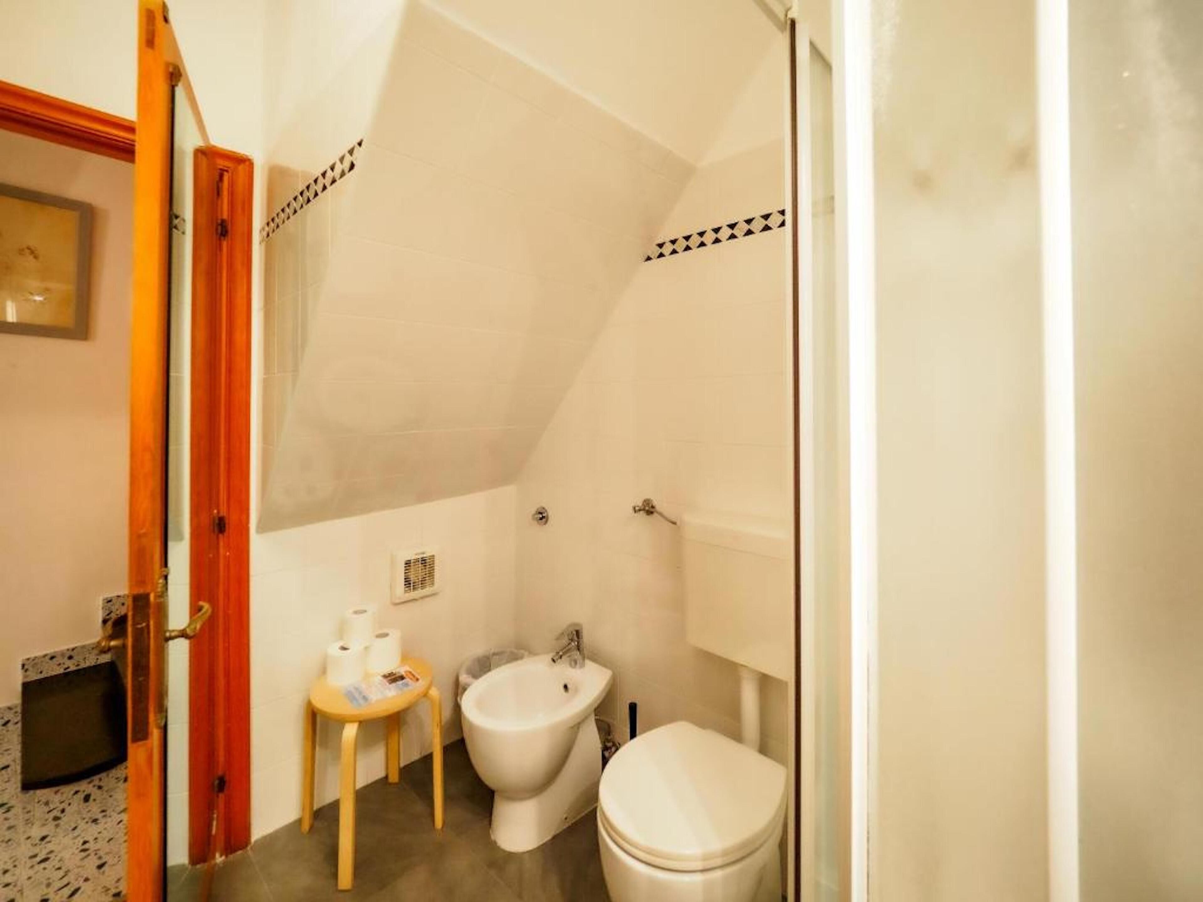 A small bathroom with a toilet, bidet, and a small table with toiletries.