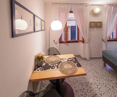 Una habitación pequeña y acogedora con una mesa de madera, dos sillas, una planta en maceta y una cama.