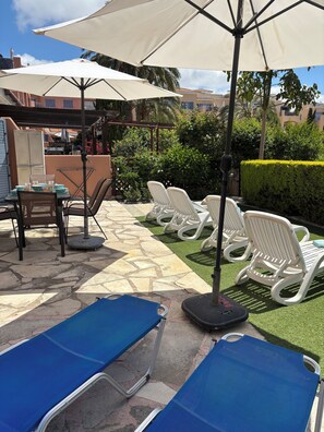Espace extérieur aménagé avec des parasols, une terrasse en pierre et un coin piscine.