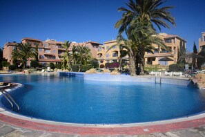 Une piscine entourée de palmiers et un bâtiment doté de balcons.