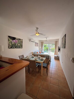 Un coin repas avec une table dressée pour quatre personnes, un ventilateur de plafond et une vue sur l’extérieur.