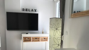 Ein modernes Wohnzimmer mit einem wandmontierten Flachbildfernseher, einem weißen Konsolentisch mit Schubladen, einer dekorativen Vase und einer Wand mit dem Schriftzug 'RELAX'.