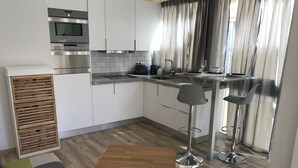 Eine moderne Küche mit weißen Schränken, Edelstahlgeräten, einem Holzschrank mit Schubladen, einer Bar mit Hockern und einem kleinen Tisch.