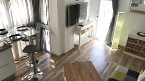 Eine moderne Küche mit Essbereich, einem an der Wand montierten Fernseher und einem kleinen Tisch mit Lampe.
