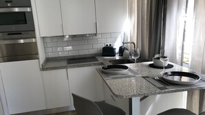 Eine moderne Küche mit weißen Schränken, einer Arbeitsplatte aus Granit und Edelstahlgeräten. Zwei Barhocker und ein Esstisch mit Tellern und Gläsern sind ebenfalls vorhanden.