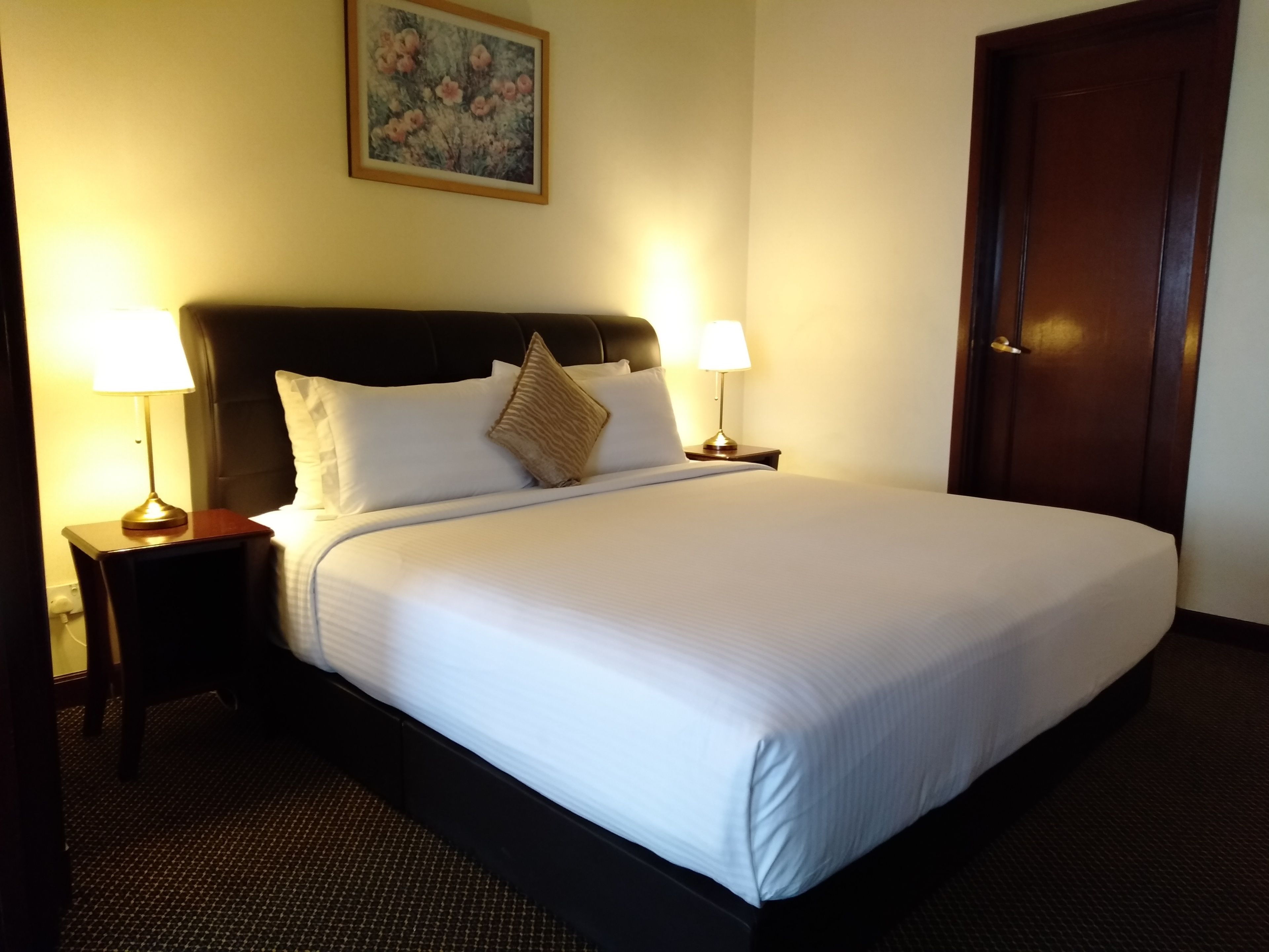 A neatly made bed with white linens, two bedside lamps, and a painting on the wall.