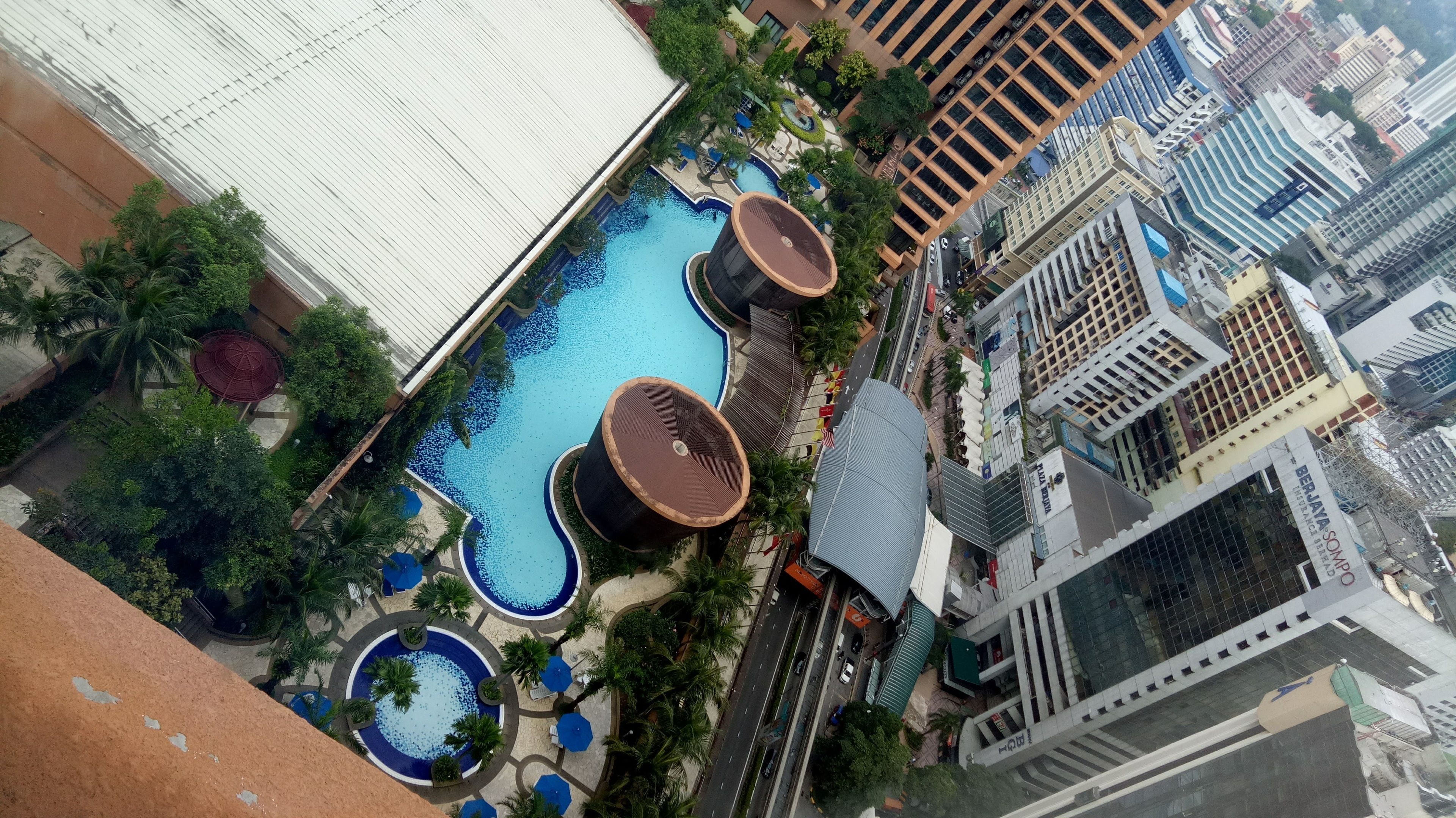 Vista aérea de un hotel con piscina, palmeras y edificios modernos al fondo.