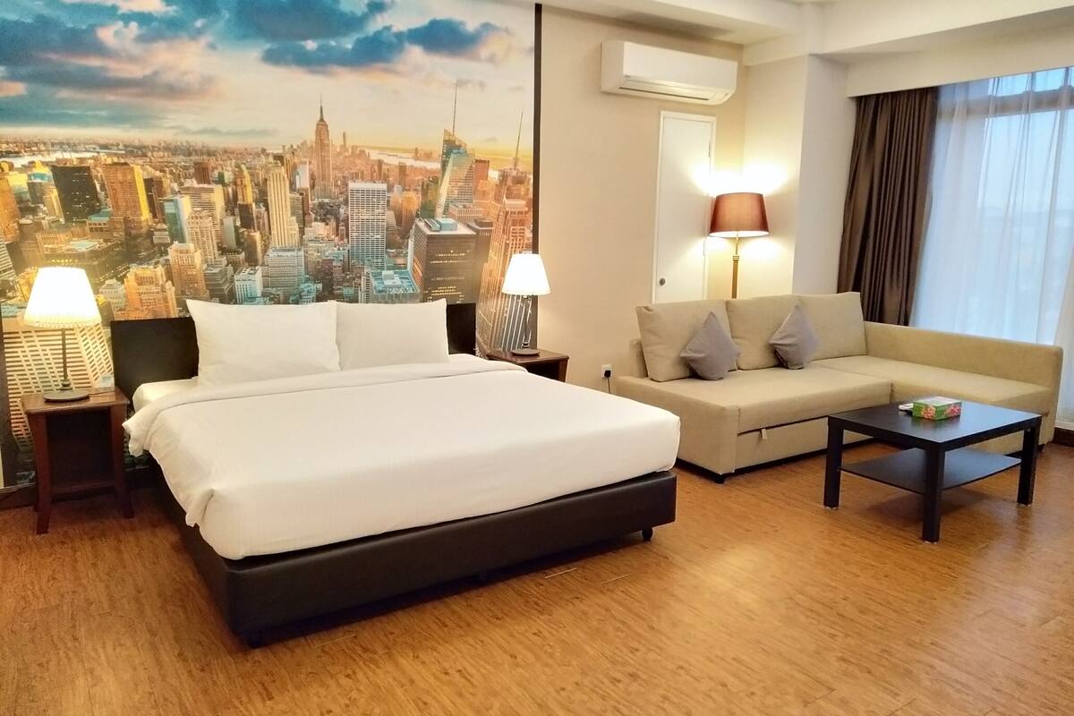 A hotel room with a bed, a sofa, a coffee table, and a cityscape mural on the wall.