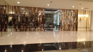 A modern lobby with a reflective floor, a patterned carpet, and a decorative partition with vertical elements. - Grand Service Apartment at Times Square (Kuala Lumpur)