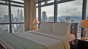 A hotel room with a large bed, two bedside lamps, and a view of a cityscape including tall buildings. - Grand Service Apartment at Times Square (Kuala Lumpur)
