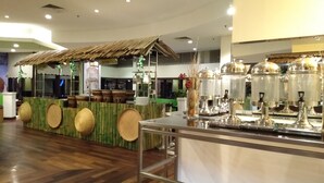 A restaurant with a wooden floor, a counter with a green backdrop, and a buffet area with food dispensers. - Grand Service Apartment at Times Square (Kuala Lumpur)