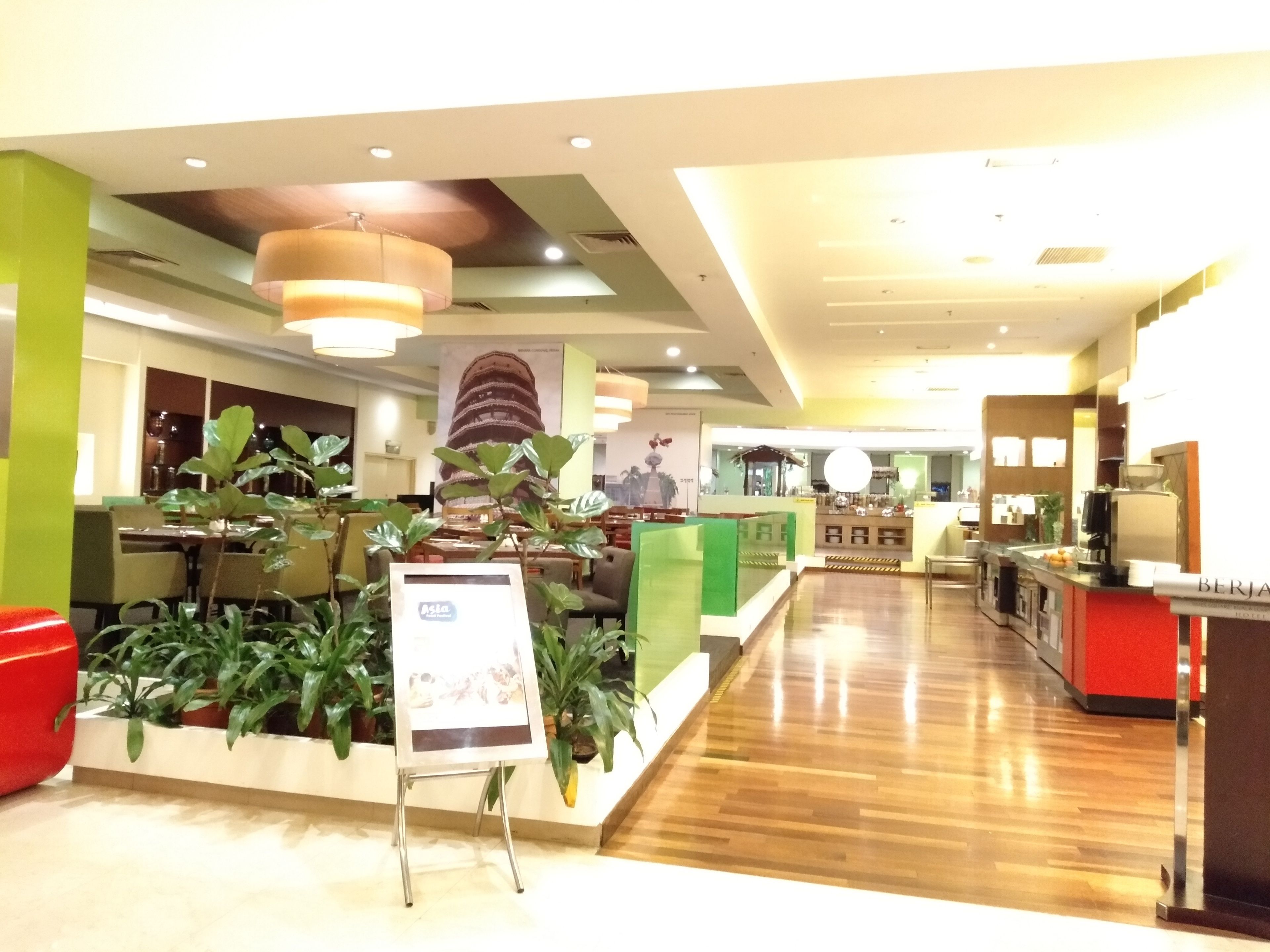 A spacious lobby with a wooden floor, green and red decor, and a large plant display.
