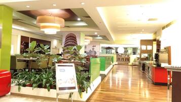 A spacious lobby with a wooden floor, green and red decor, and a large plant display.