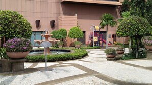 A modern building with a courtyard featuring a fountain, potted plants, and a playground. - Grand Service Apartment at Times Square (Kuala Lumpur)