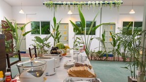 A dining area with a long table set for a meal, surrounded by potted plants and a view of a building with numbered doors. - Sky View Bed & Breakfast (Yangon)