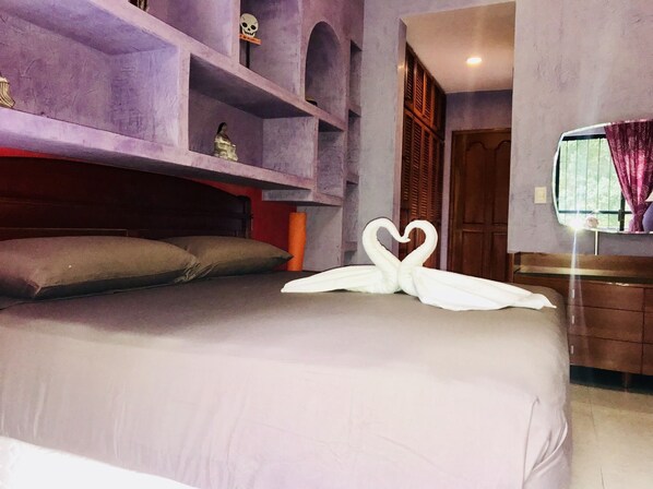 A bedroom with a bed, a headboard, a shelf with a skull decoration, a window with curtains, and a mirror.