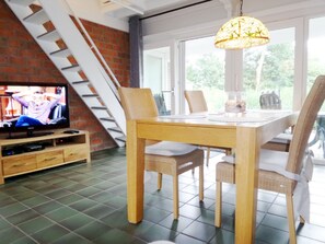 Relax in this stylish living room with a dining table for four, TV, and glass door leading to an outdoor area.