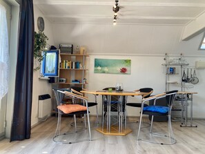 A dining area with a wooden table, four chairs, a bookshelf, a clock, and a painting.