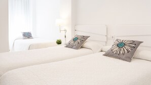 A hotel room with two beds, each with a white quilted bedspread and a gray pillow with a blue flower design. There is a small potted plant on the nightstand and a wall-mounted lamp. - New Condo in the best Resort, Modern decoration - only families (Playa de Gandía)
