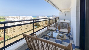A balcony with wicker furniture, a small table, and a view of buildings and the sea. - New Condo in the best Resort, Modern decoration - only families (Playa de Gandía)