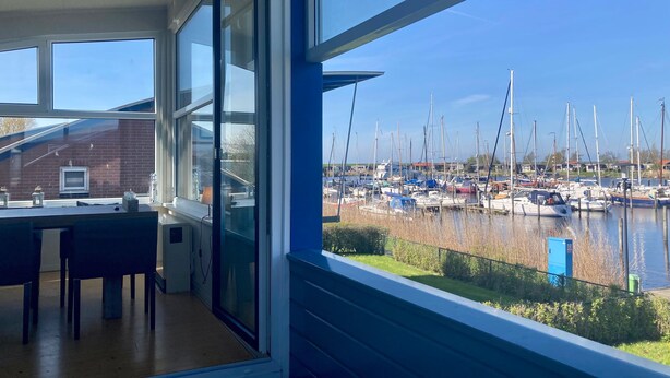 Une pièce dotée d’une grande fenêtre donnant sur une marina où sont amarrés des bateaux.