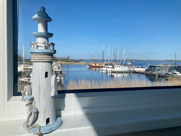 A lighthouse with a rope wrapped around it, a calm water body with boats, and a clear sky.