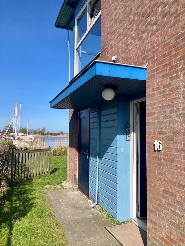 A two-story building with a blue exterior, a visible number '16' on the side, and a door leading to a covered entrance. - 6 pers harbor house Nirvana on the marina with lake view and sauna (Anjum)