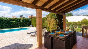 Une terrasse extérieure avec une piscine, des meubles en osier et une table préparée pour le petit-déjeuner.