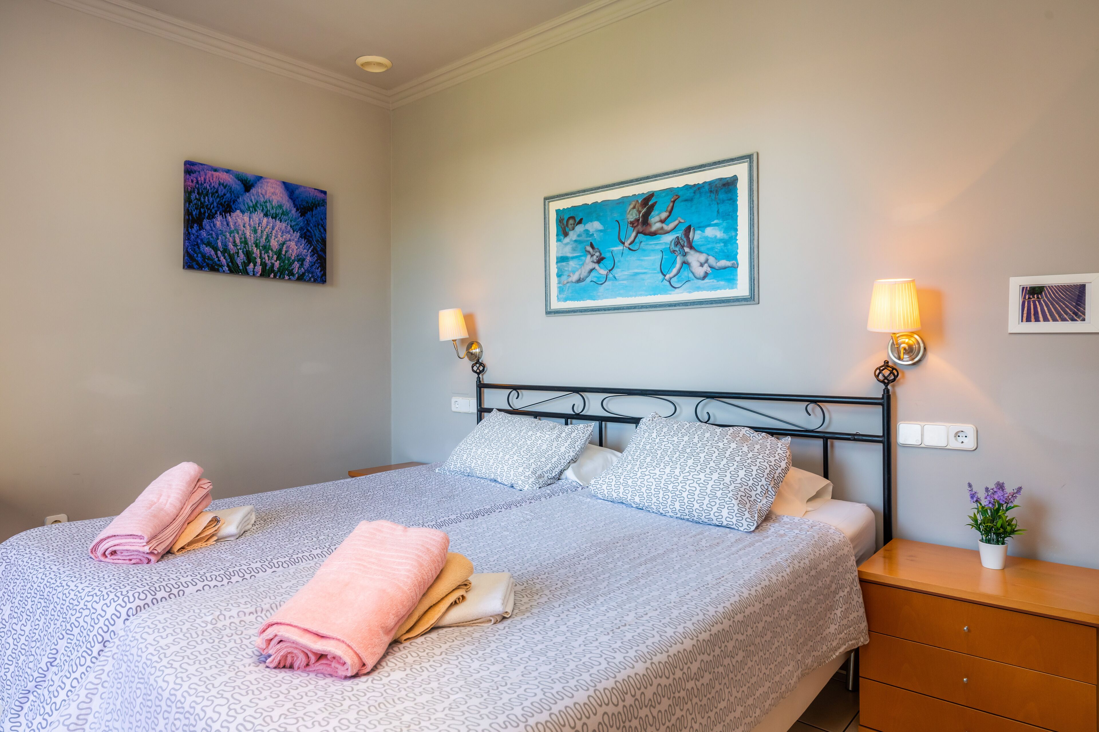A neatly made bed with pillows and folded towels, a nightstand with a lamp, and a small plant.