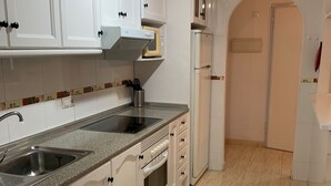 Een keuken met witte kastjes, een granieten aanrechtblad, een inbouwoven en een koelkast.