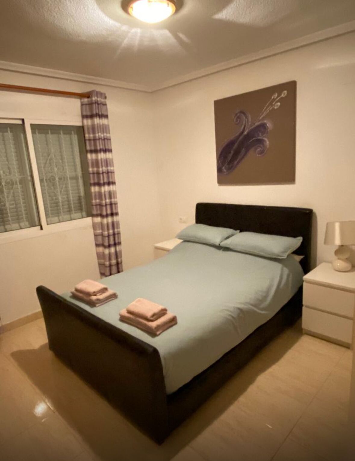 A bedroom with a bed, nightstands, a window with curtains, and a wall art piece.