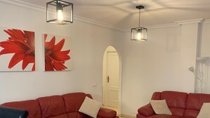 Een woonkamer met twee rode leren banken, een houten salontafel en een bruin vloerkleed. Er zijn twee wandlampen en twee grote rode schilderijen met bloemenmotieven.