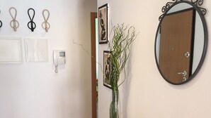 Un pasillo con un espejo redondo, un florero con plantas y una cesta tejida sobre una mesita.