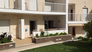 Un edificio residencial de varios pisos con balcones, un pequeño jardín y una puerta que da a un garaje.