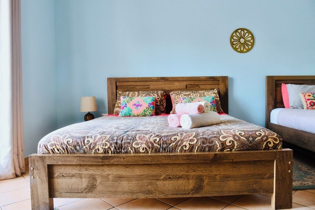 Una cama de madera con ropa de cama estampada, una lámpara de noche y un adorno en la pared.