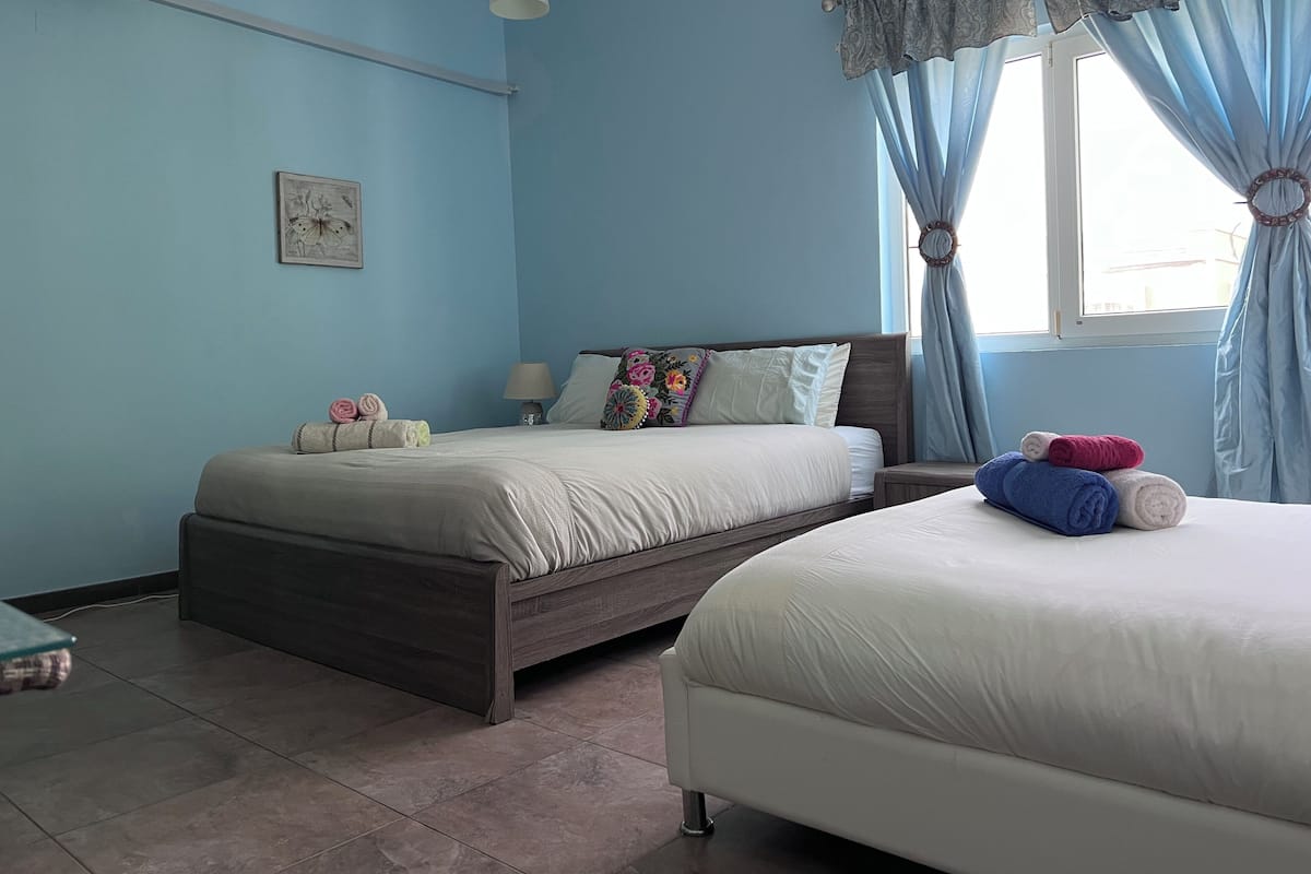 A bedroom with two beds, a bedside table, a lamp, and a window with curtains.