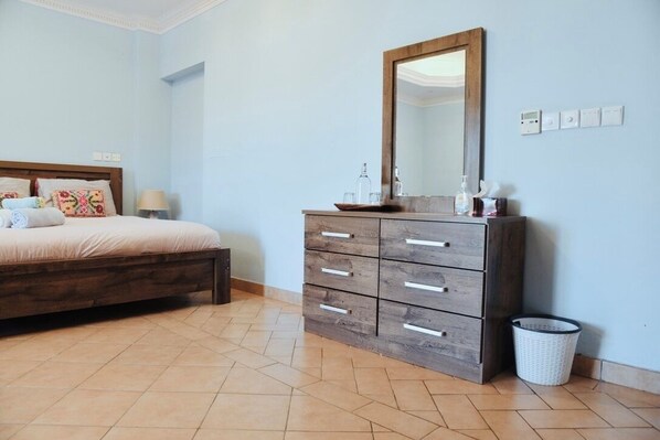 A bedroom with a bed, a wooden dresser with drawers, a mirror, and a waste basket.
