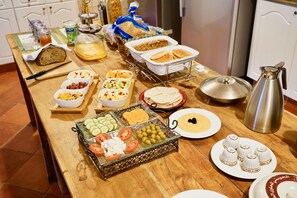 A breakfast buffet with various food items and a coffee pot on a wooden table.