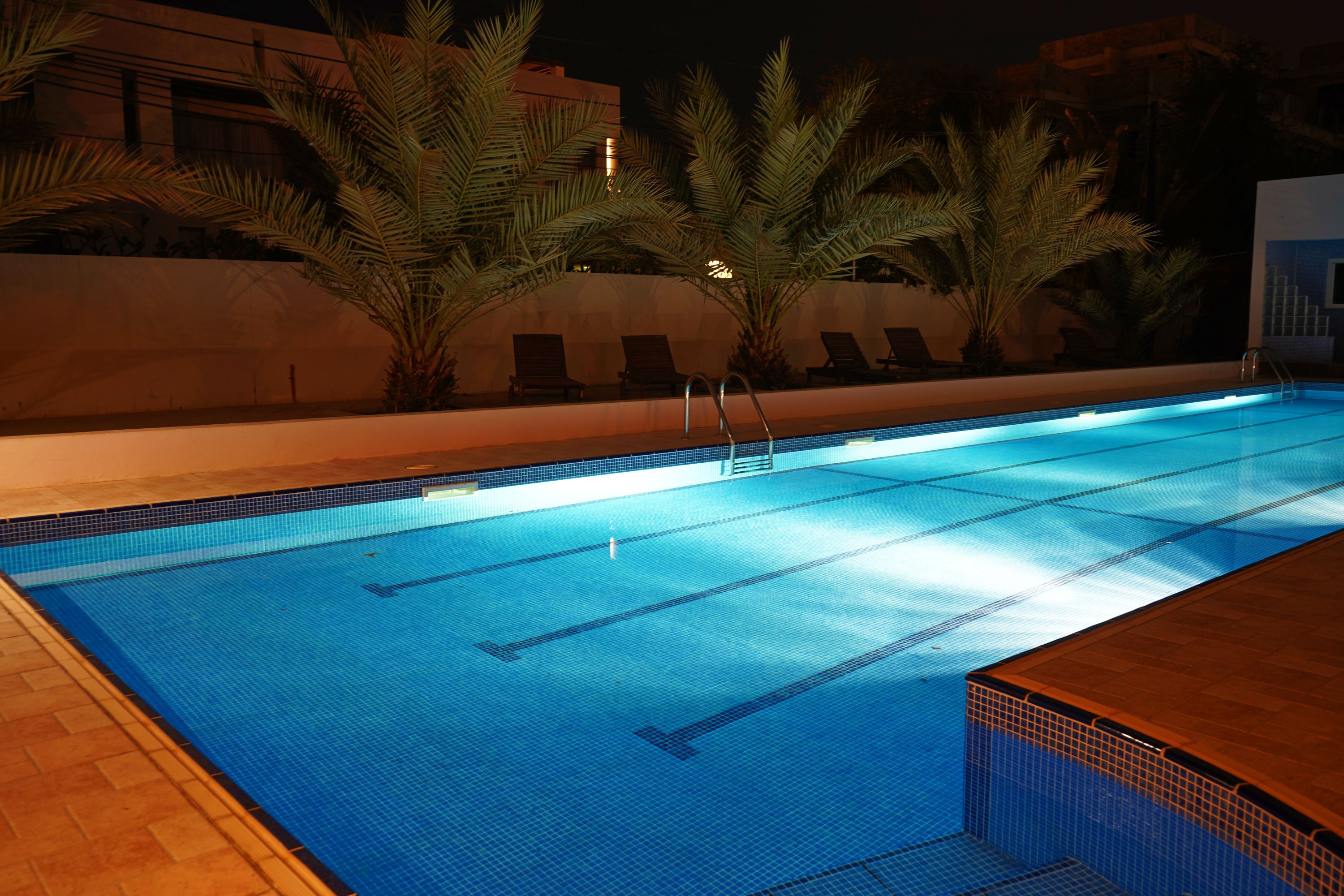 A swimming pool with clear lane markings, surrounded by palm trees and lounge chairs, indicating a resort setting.