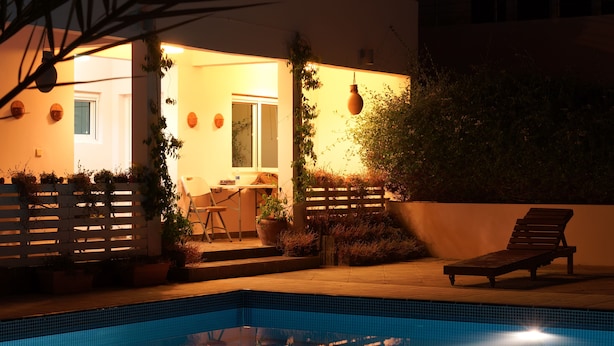 Une piscine avec une terrasse en bois, une chaise longue et des plantes en pot.
