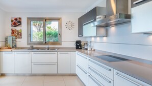 A modern kitchen with white cabinets, a stainless steel range hood, and a window with a view of greenery.