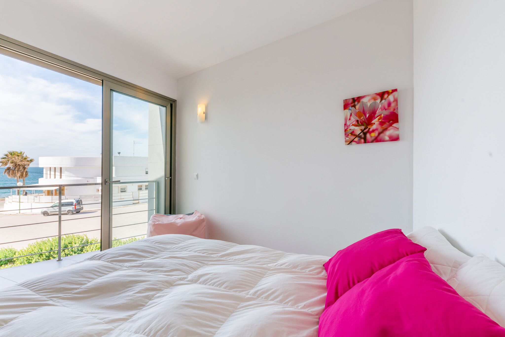 Une chambre à coucher avec un lit, une fenêtre, une lampe fixée au mur et un tableau.