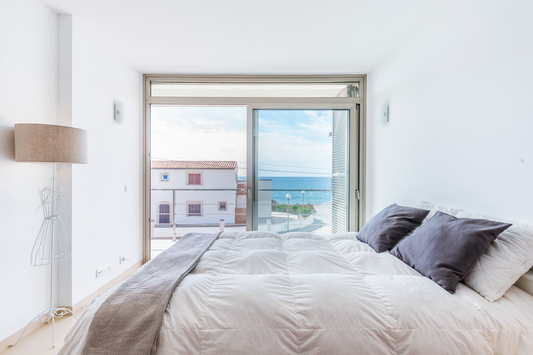 Une chambre à coucher avec un lit, une lampe et une vue sur la mer, visible à travers une porte vitrée.