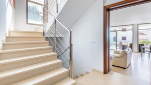 A modern interior with a staircase leading to a second floor, a living area with a sofa and a dining table, and a view of the outdoors.