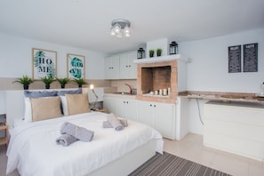 A modern hotel room with a bed, a small kitchenette, and a bathroom.