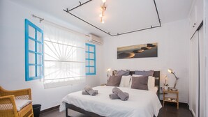 Ein modernes Schlafzimmer mit einem großen Bett, einem Korbstuhl, einem Nachttisch mit Lampe und einem Fenster mit blauen Fensterläden.
