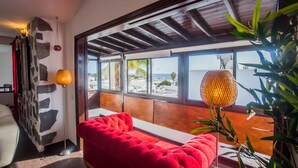 Ein Zimmer mit einem roten Sofa, einer Steinsäule und Blick aufs Meer.