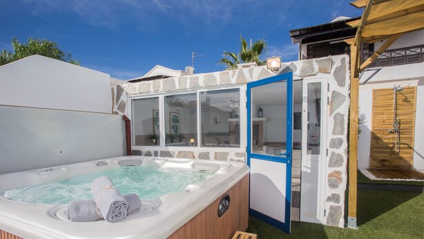 Ein Whirlpool mit Holzverkleidung, einer Steinwand und einer blauen Tür, die auf ein Holzdeck führt.