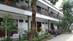 A multi-story building with a white facade, potted plants on balconies, and a row of parked motorcycles. - Mandala Hotel (Tangerang)