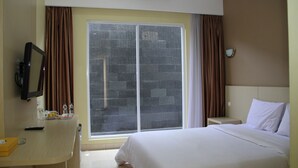A hotel room with a bed, a desk with a chair, a television, a window with curtains, and a nightstand. - Mandala Hotel (Tangerang)